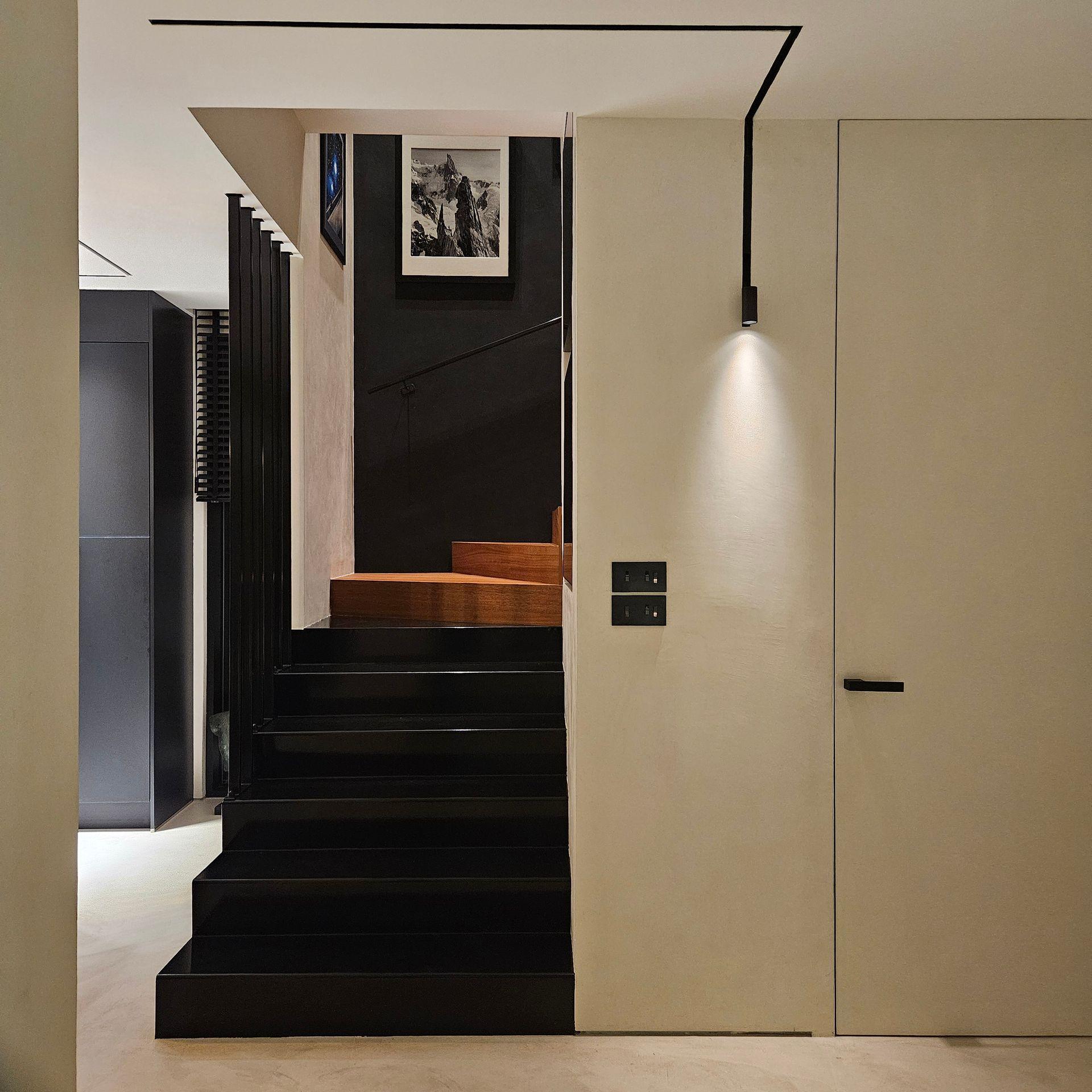 Modern interior with black stairs, framed photos, and minimal lighting.